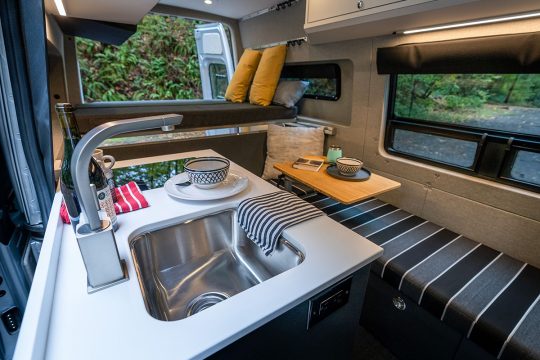 Interior look at a custom van with the kitchen sink and faucet upfront, one long bench seat along driver-side wall