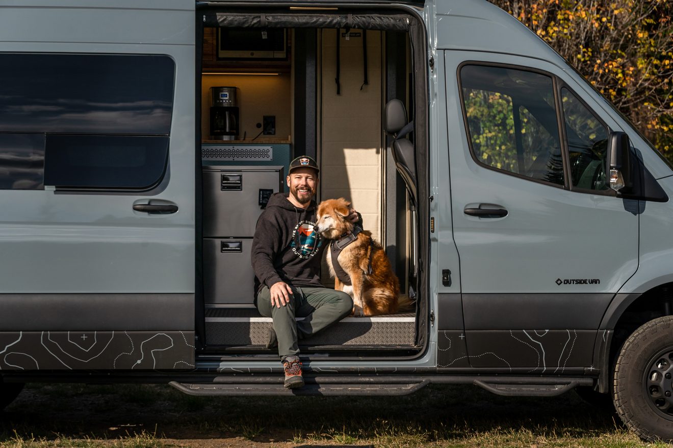 Man and dog sitting together in a van's open passenger-side slider door