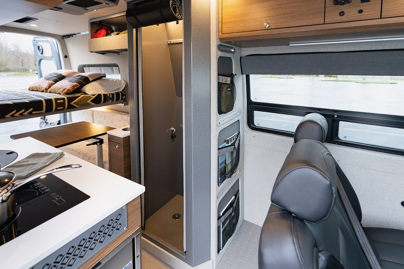 Van interior showing a kitchen on the left and enclosed shower on the right with sleeping in the back