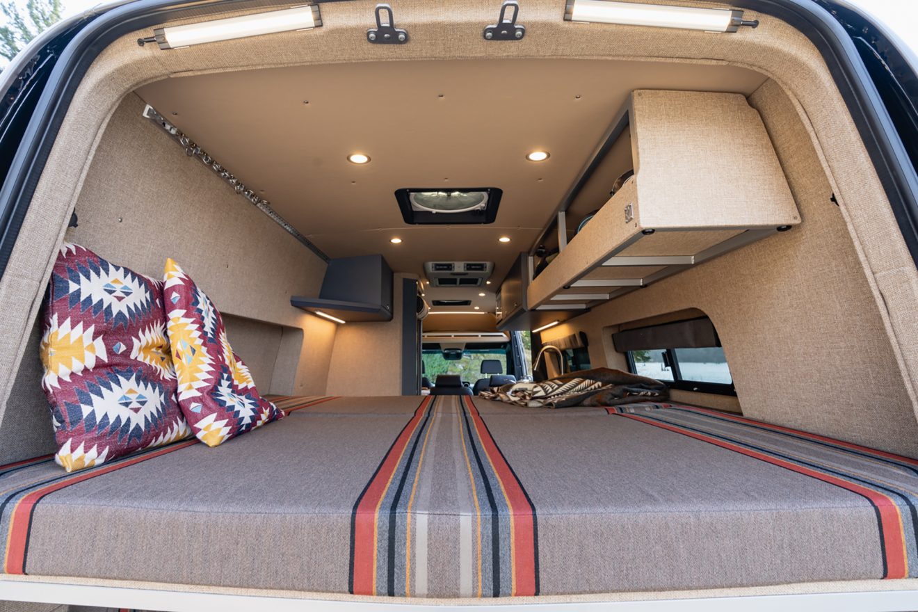 Rear van interior raised panel bed beneath open overhead cabinet
