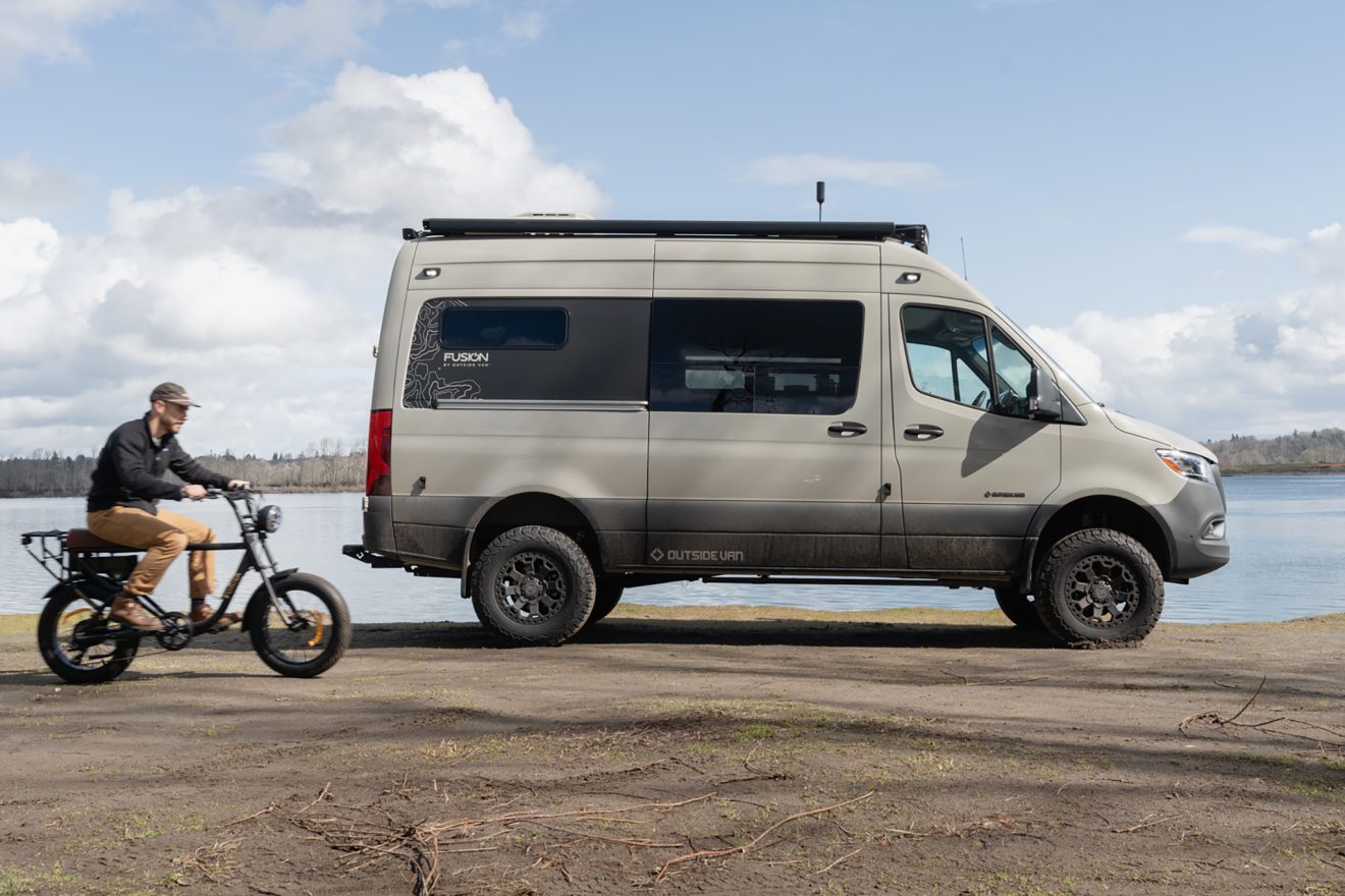 Small white van with the passenger-side slider door open parked next to a large pond