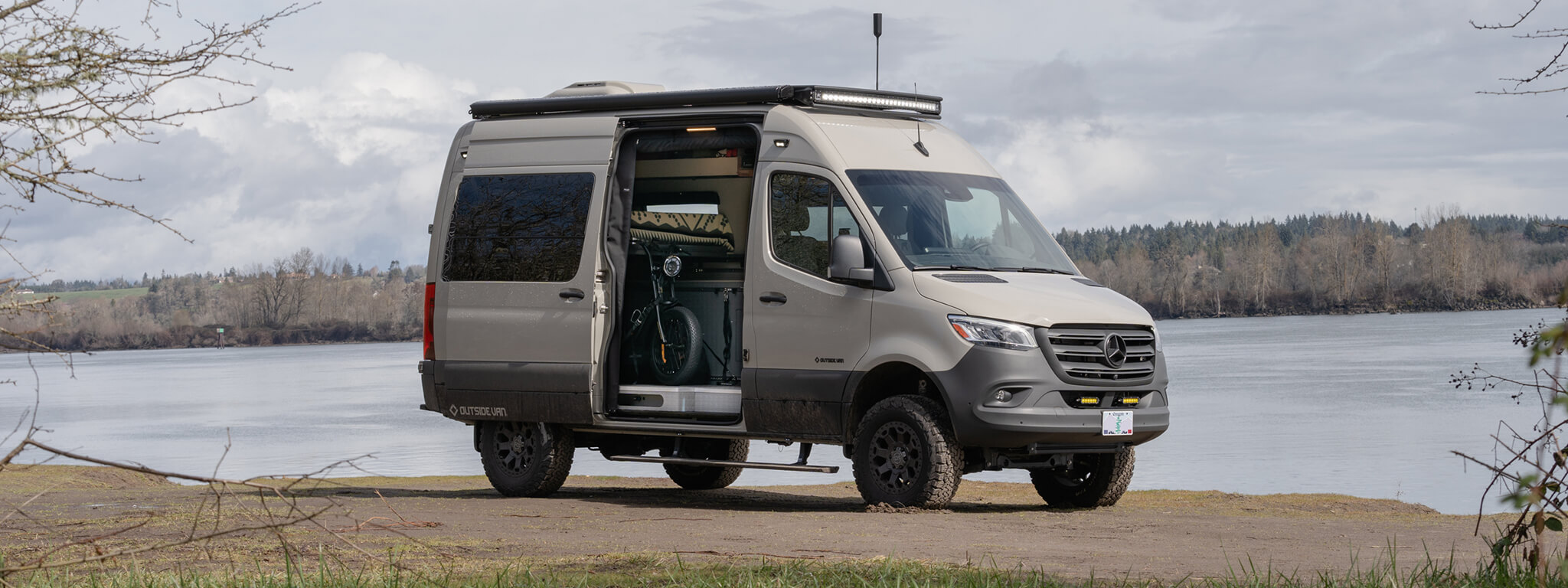 Small white van with the passenger-side slider door open parked next to a large pond