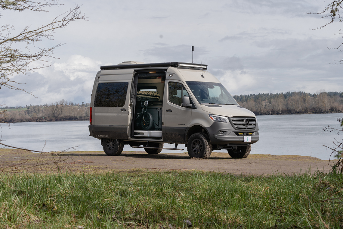 Small white van with the passenger-side slider door open parked next to a large pond