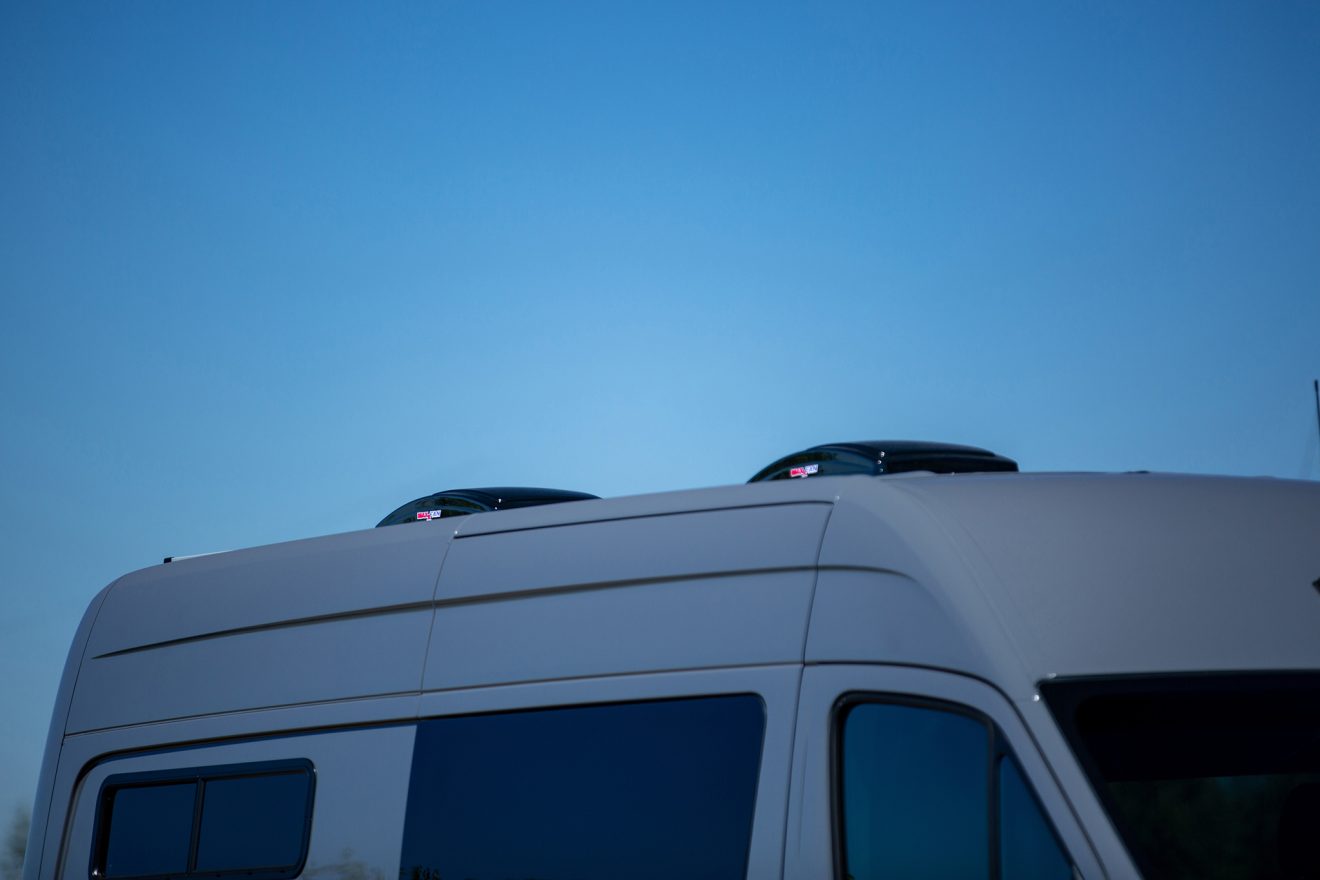 Detail of dual roof mounted maxxair fans on custom off road 144 sprinter van in sunny gravel parking lot