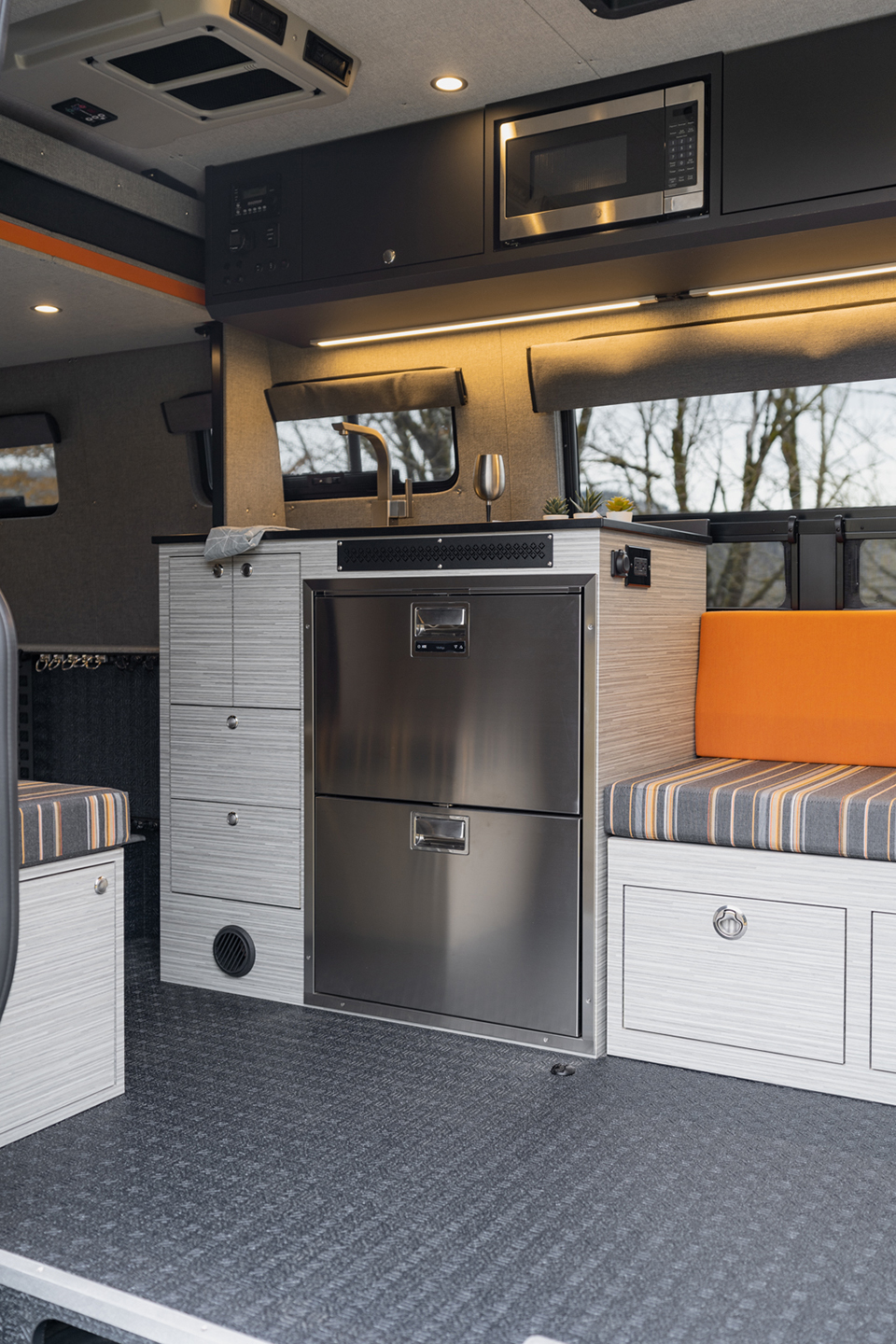 Van cabin interior with custom orange and grey striped upholstery next to vitrifrigro stainless steel refrigerator