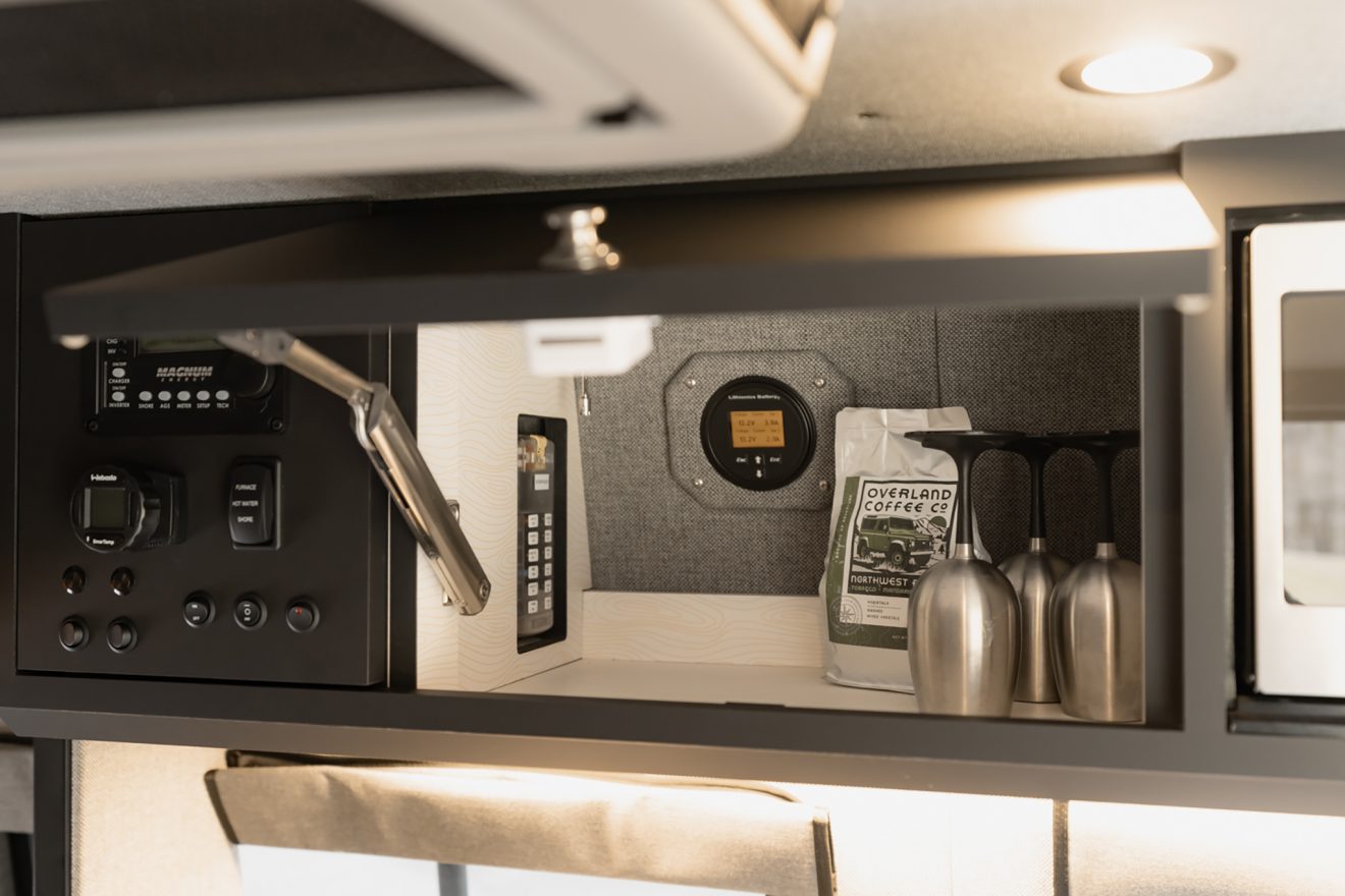 Open overhead cabinetry with wine glasses next to power control system