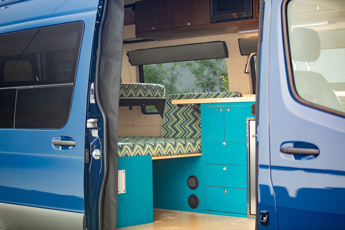 Custom interior with bed, kitchen, and bench inside converted sprinter van