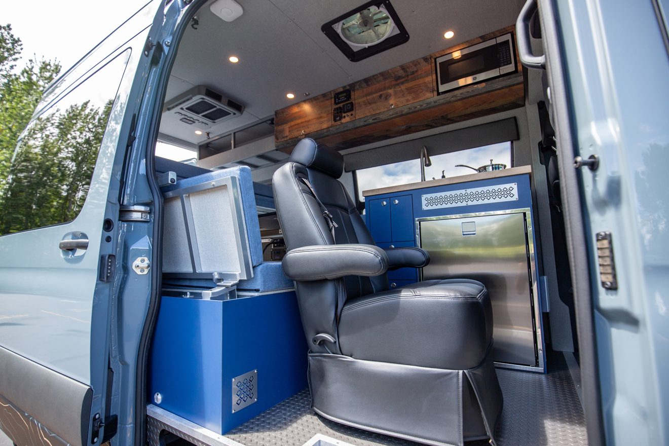 Interior image of custom off road sprinter van with bed, shelves, air compressor, shower and kitchen in a grey and blue color scheme