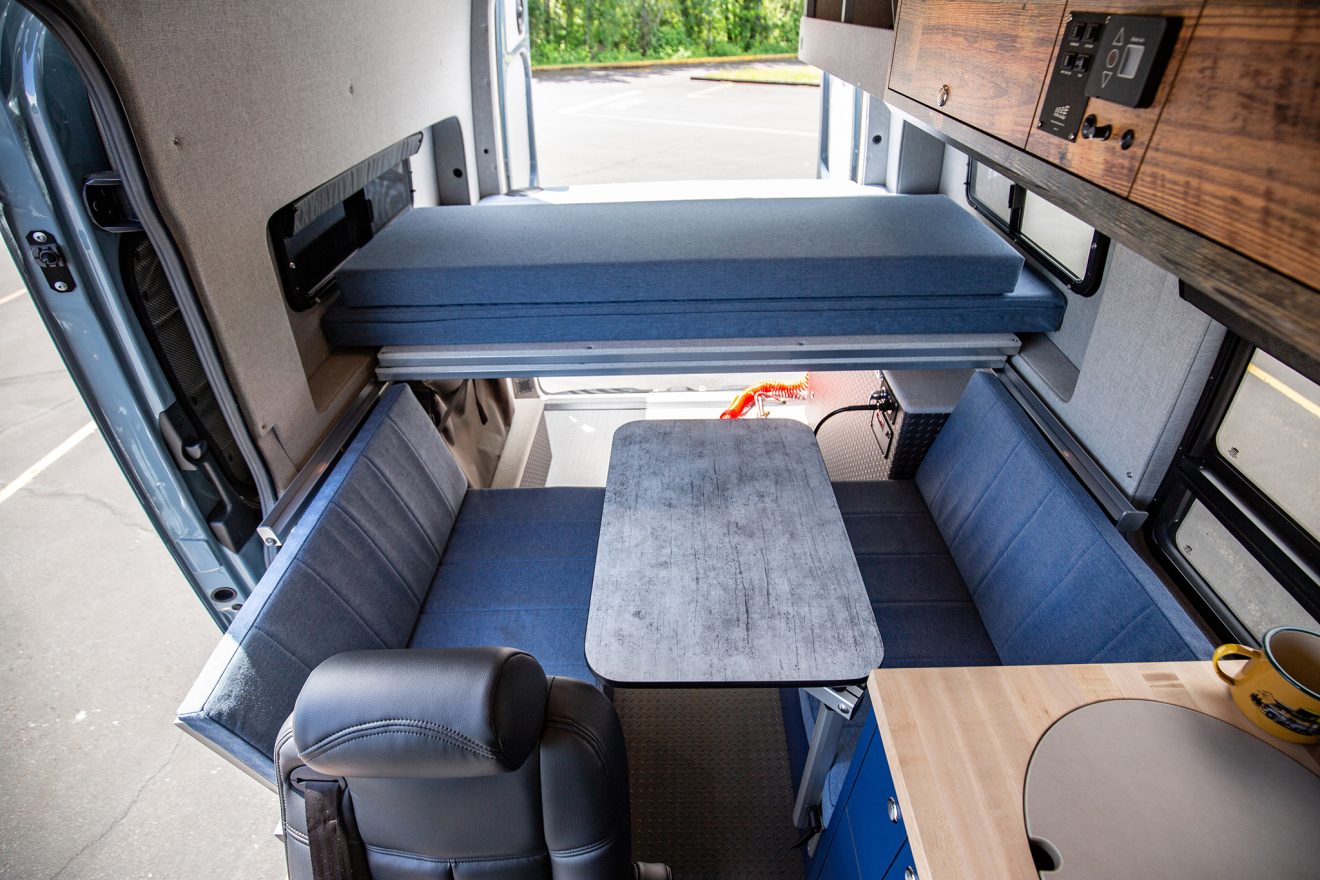 Detail interior image of custom off road sprinter van with table, kitchen, and blue and dark wood cabinetry