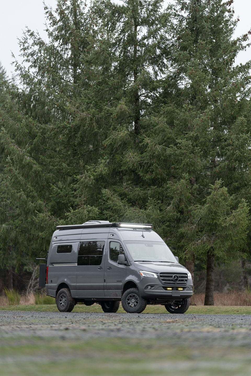 Front of a Grey van in a field with a passenger-side slider closed beneath a fiamma awning and 50 inch rigid industries light bar