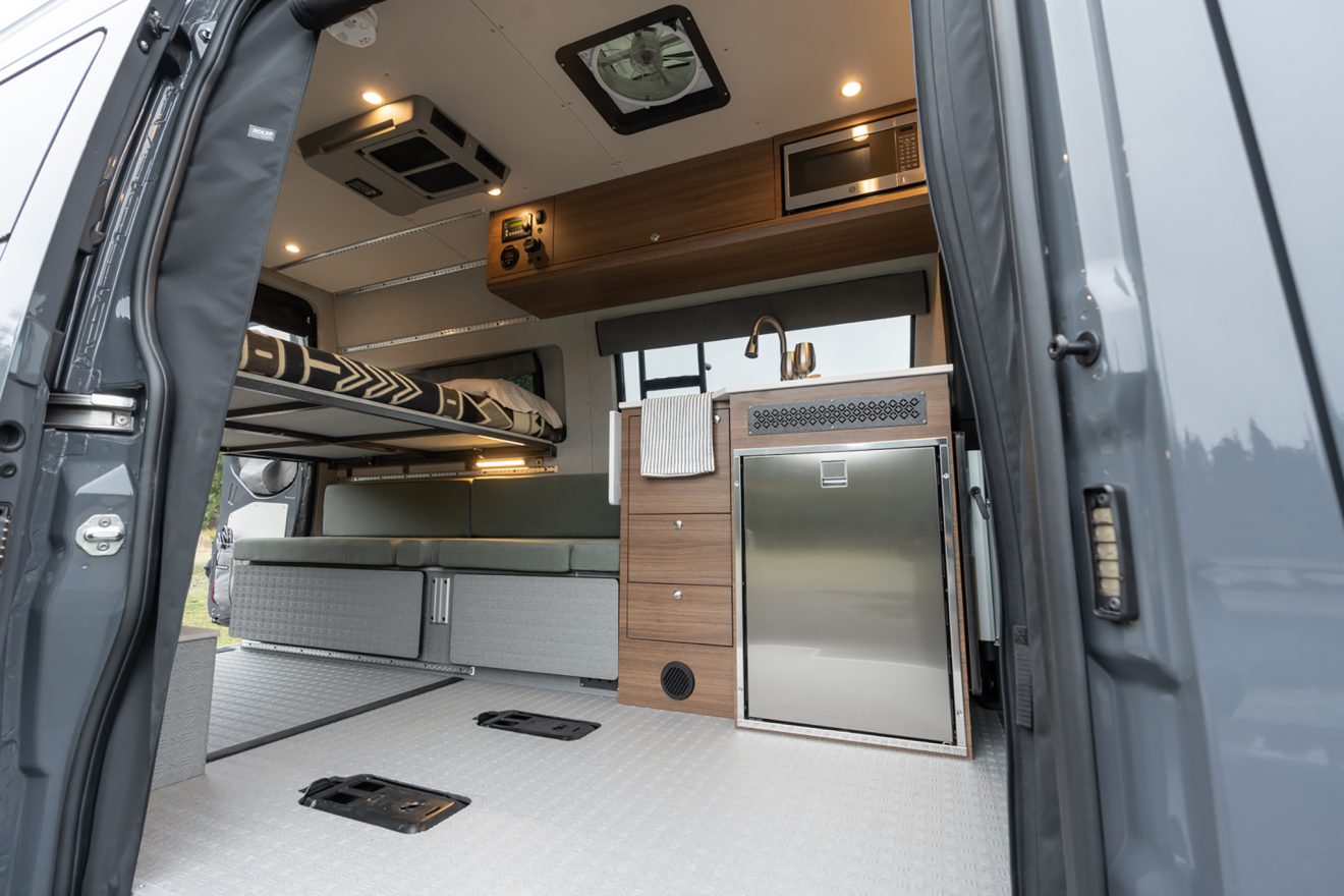 Passenger-side slider door opening into a galley kitchen with refrigerator, upper sleeping platform, and lower bench seat