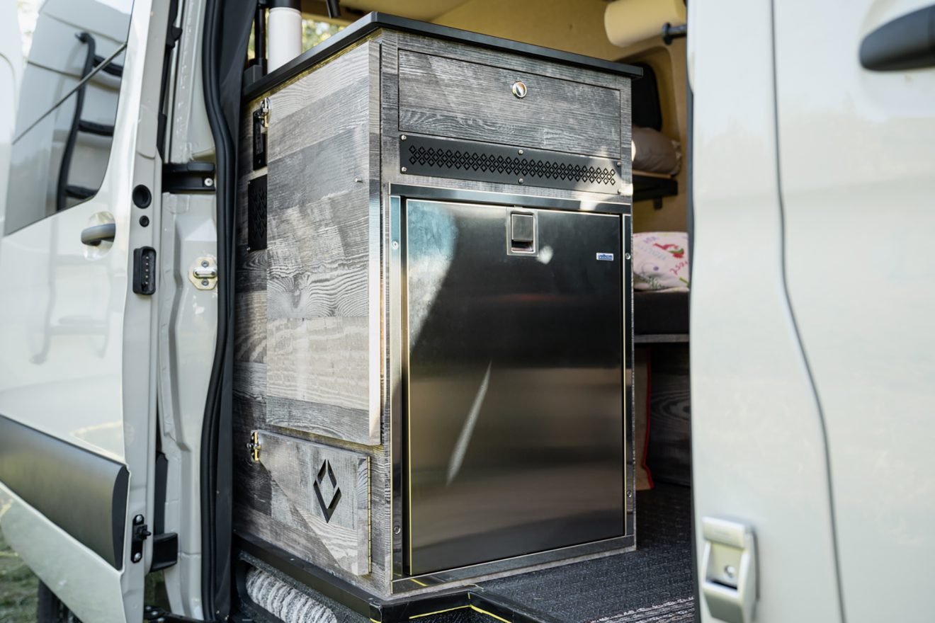 Passenger slider door with dropdown table and stainless steel refrigerator inside a sprinter van