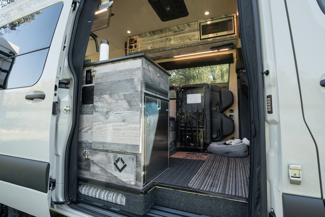 Passenger slider door with dropdown table and stainless steel refrigerator inside a sprinter van