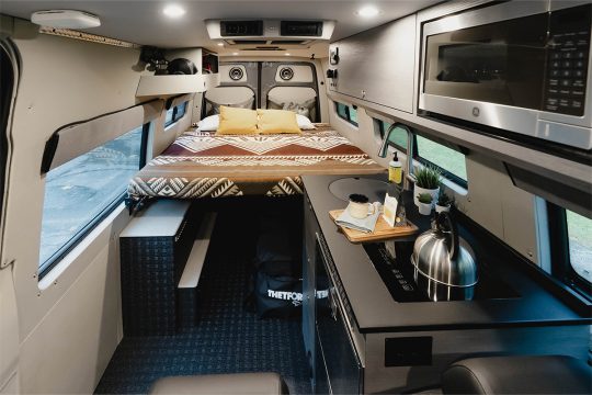 Interior of a van with a kitchen galley on the right side and a large raised bed platform in the back