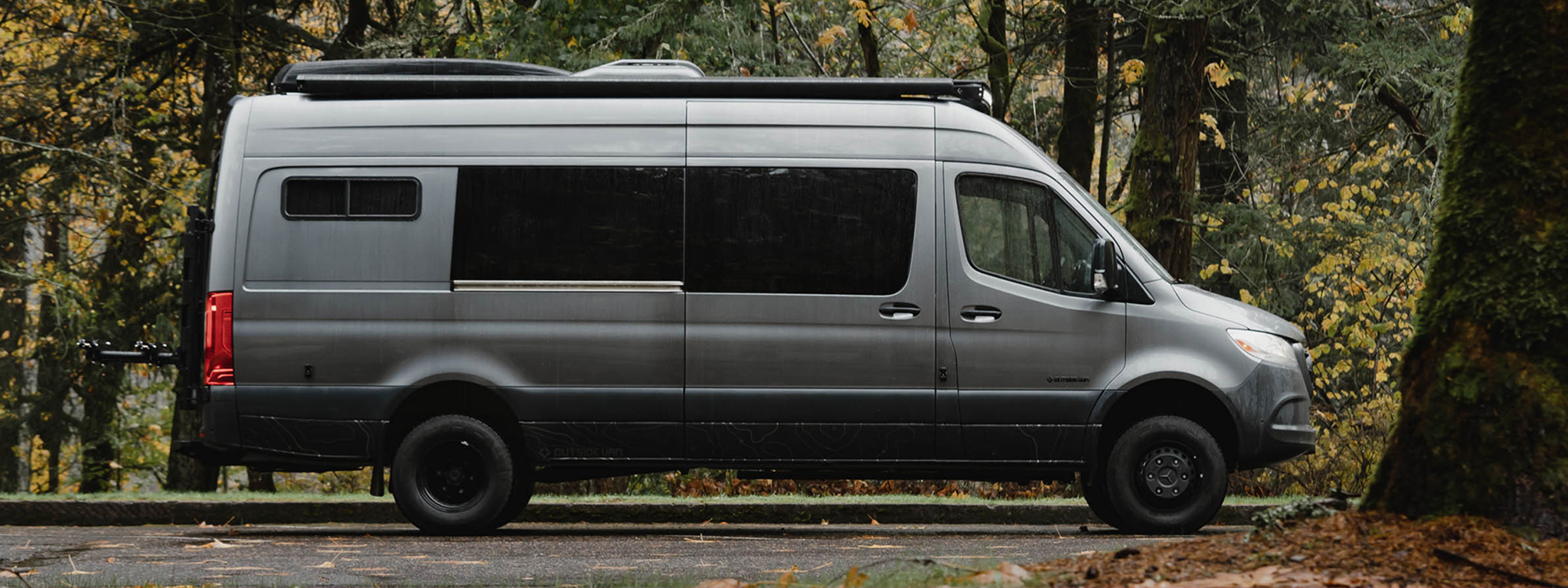 the exterior of a large grey van parked in a dark forest