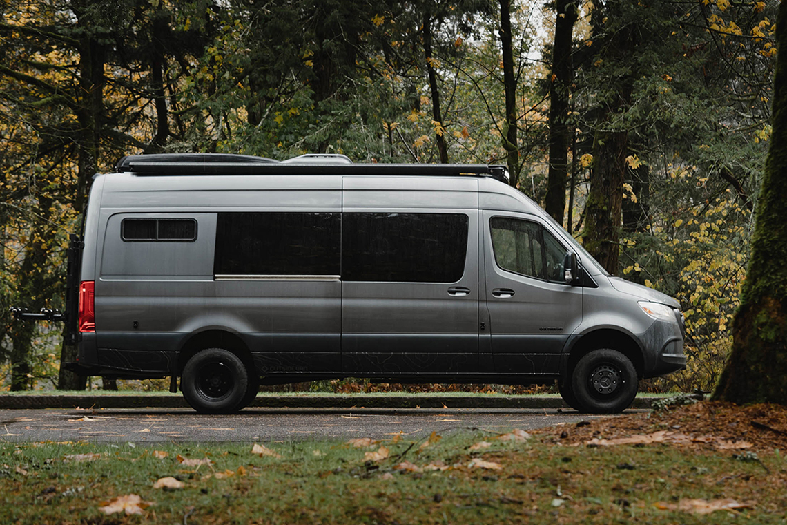 the exterior of a large grey van parked in a dark forest