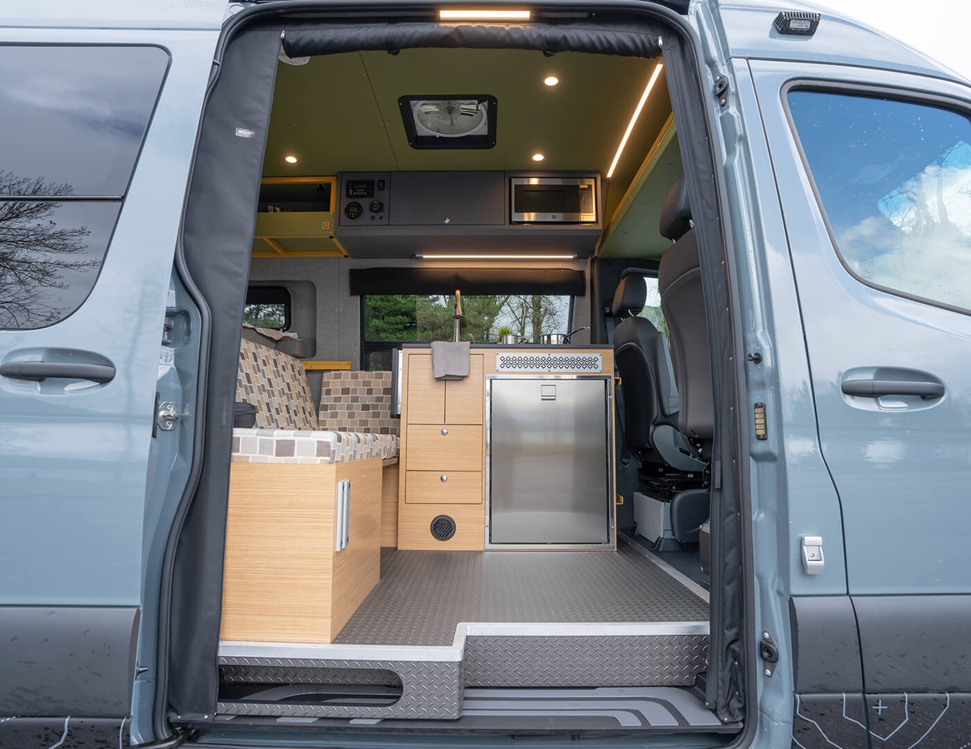 Open passenger slider door with bench sofa, kitchen with sink and burner on the right