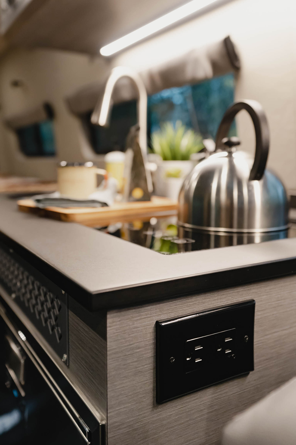 Black countertop with black outlet, one induction burner with a silver tea kettle on top