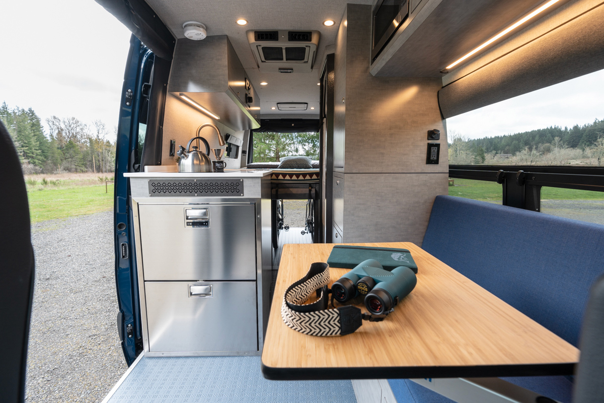 Interior image of custom off road mercedes sprinter van with full kitchen, table, cabinetry, and blue and grey color scheme
