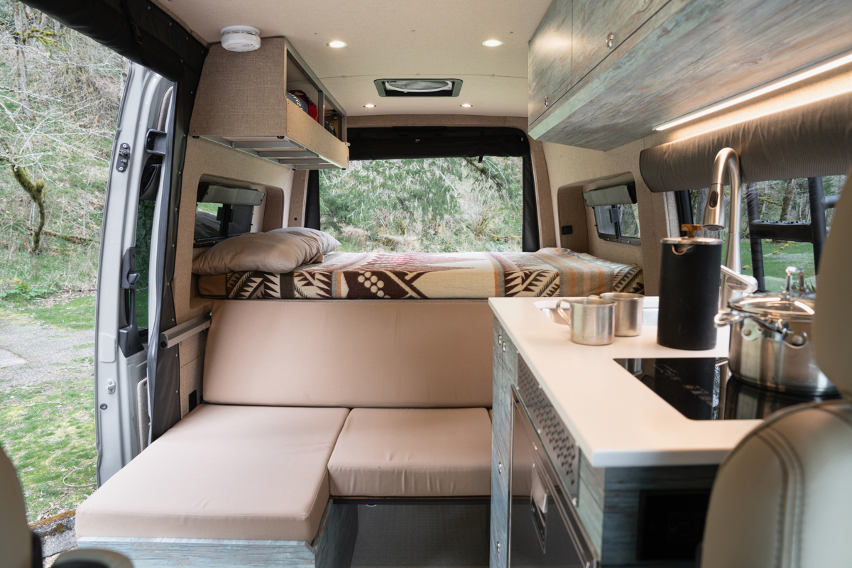 custom mercedes sprinter van conversion with couch, kitchen galley, tan upholstery, and blue cabinetry