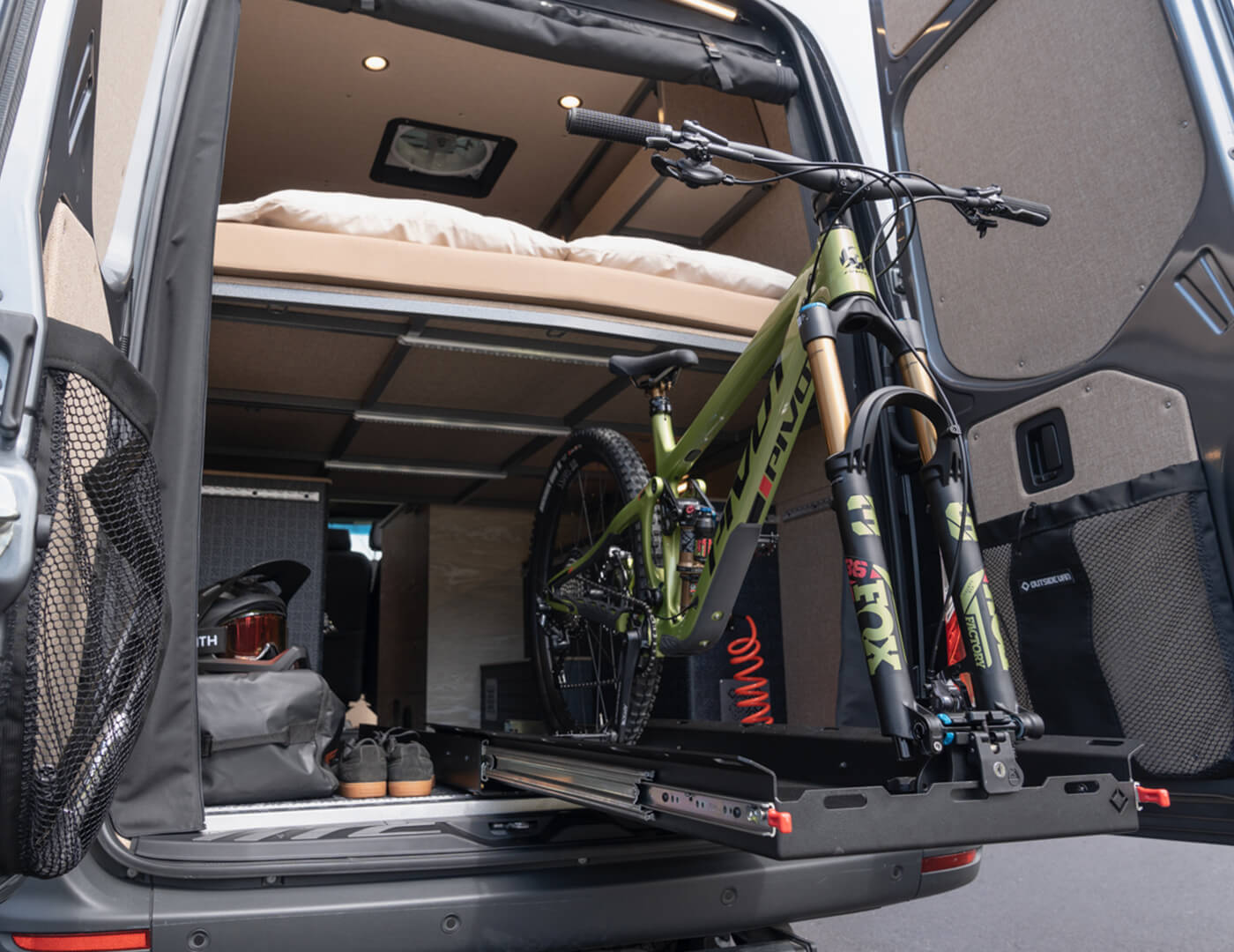 Green pivot mountain bike on an outside van gear glider slide out tray in the garage of a custom converted sprinter van