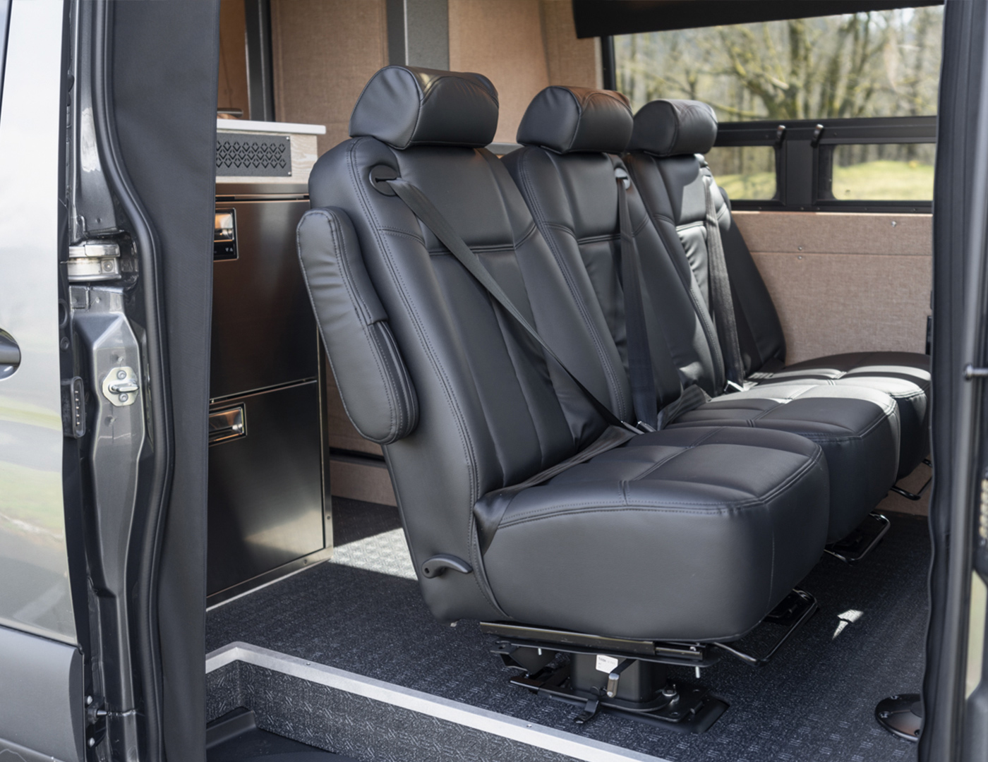 Custom converted mercedes sprinter by outside van with black floor, seating for five, and refrigerator